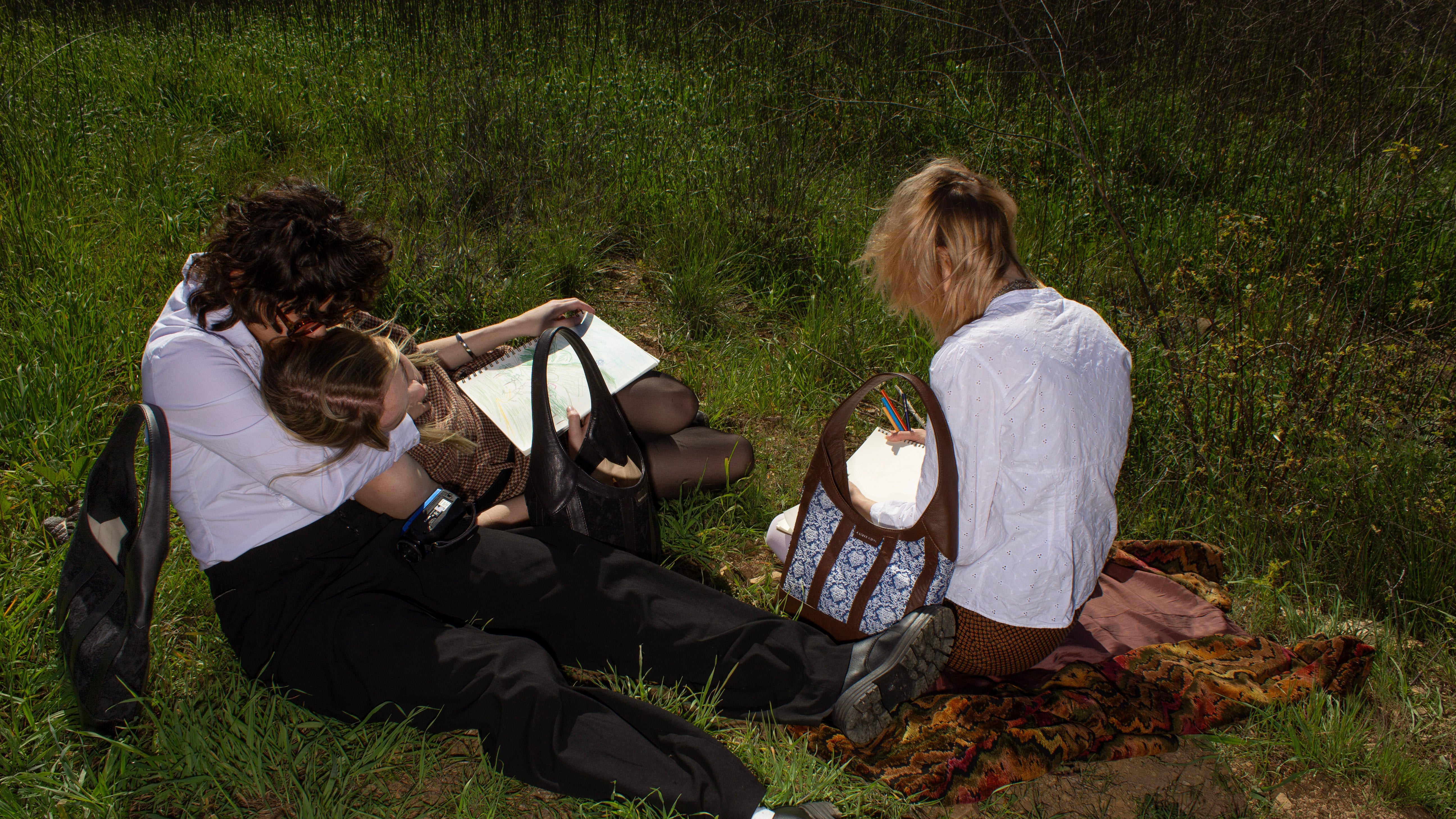 three people sitting in a grassy field