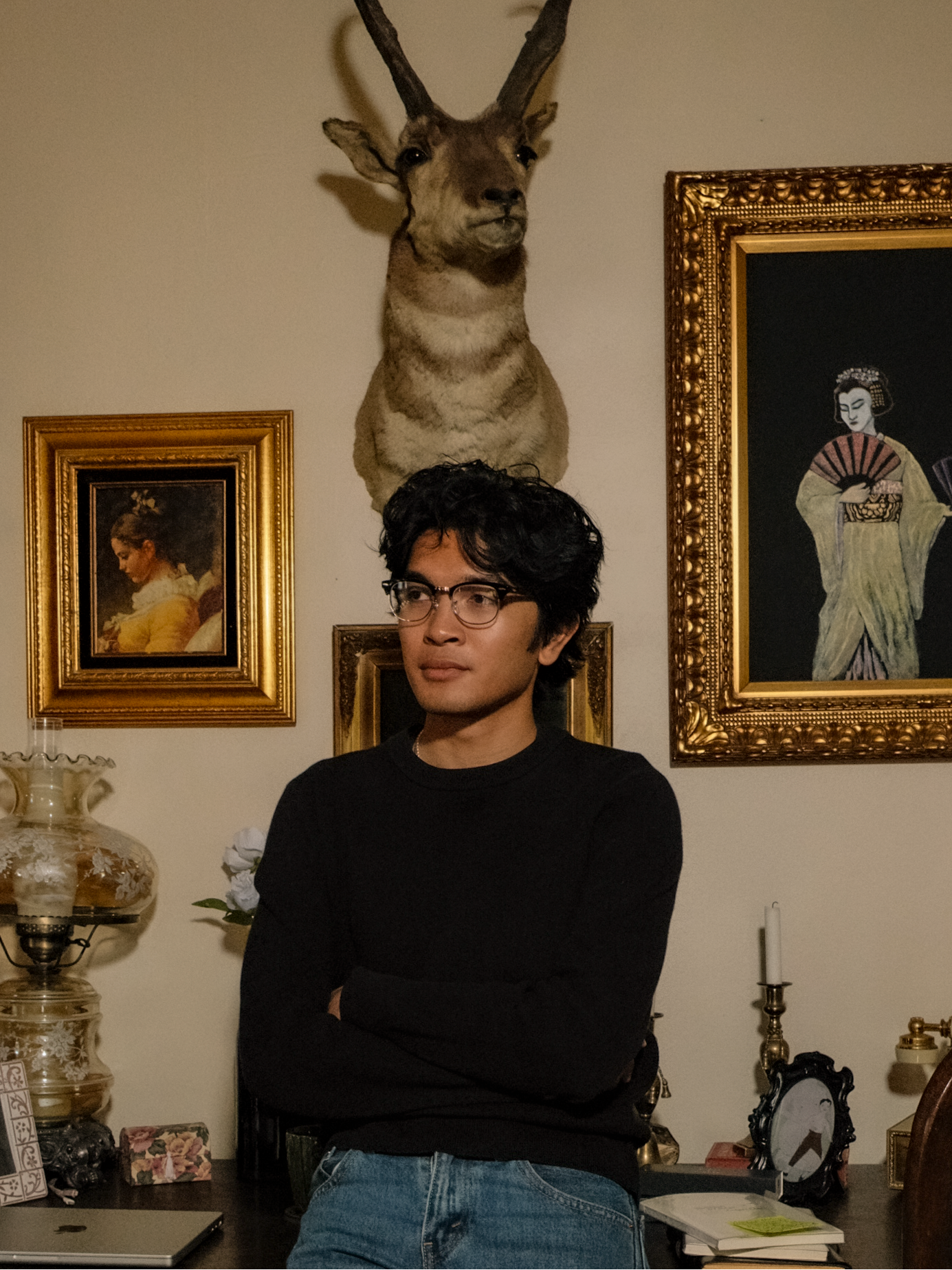 Casper Choa standing in a room with a mounted animal head and framed pictures on the wall.