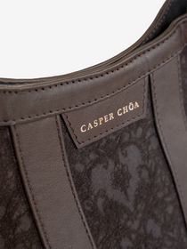Close-up of a silver-tone CASPER CHOA stamped signature on a back leather handbag with black/black heart-patterned jacquard on a white background